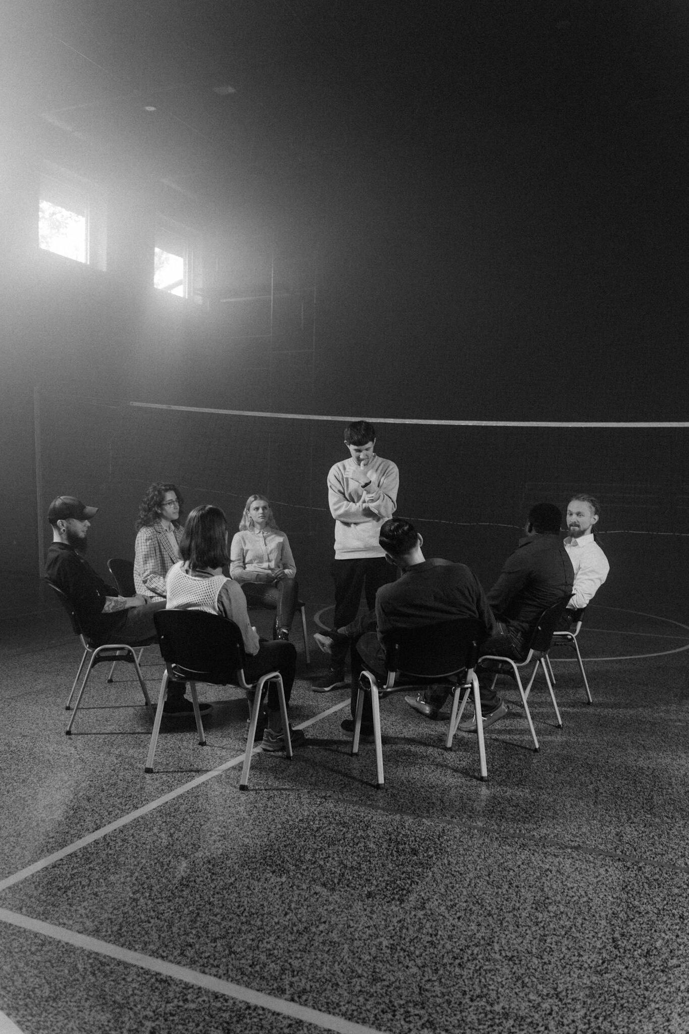 A diverse group in therapy, seated in a large room with natural light.